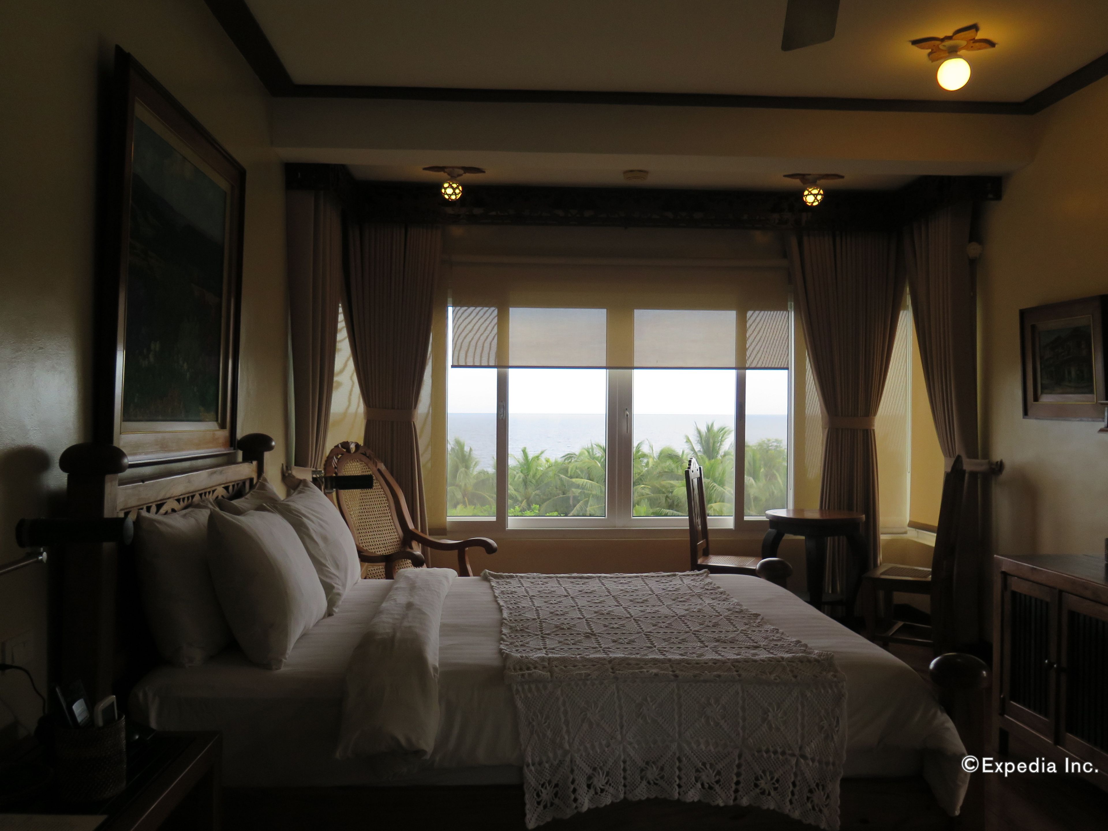 A bedroom with a large bed, a wooden headboard, a view of the ocean, and a ceiling fan.
