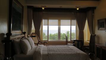 A bedroom with a large bed, a wooden headboard, a view of the ocean, and a ceiling fan.