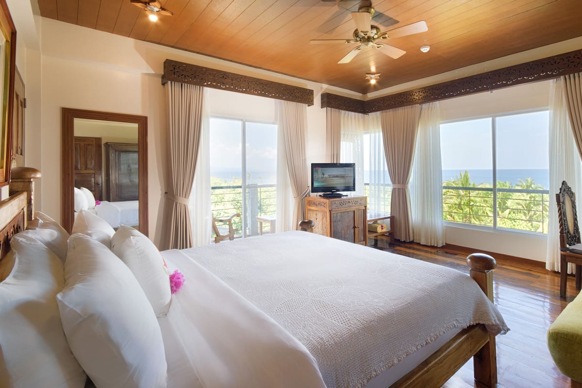 A spacious bedroom with a large bed, a television, and a balcony with a view of the ocean.