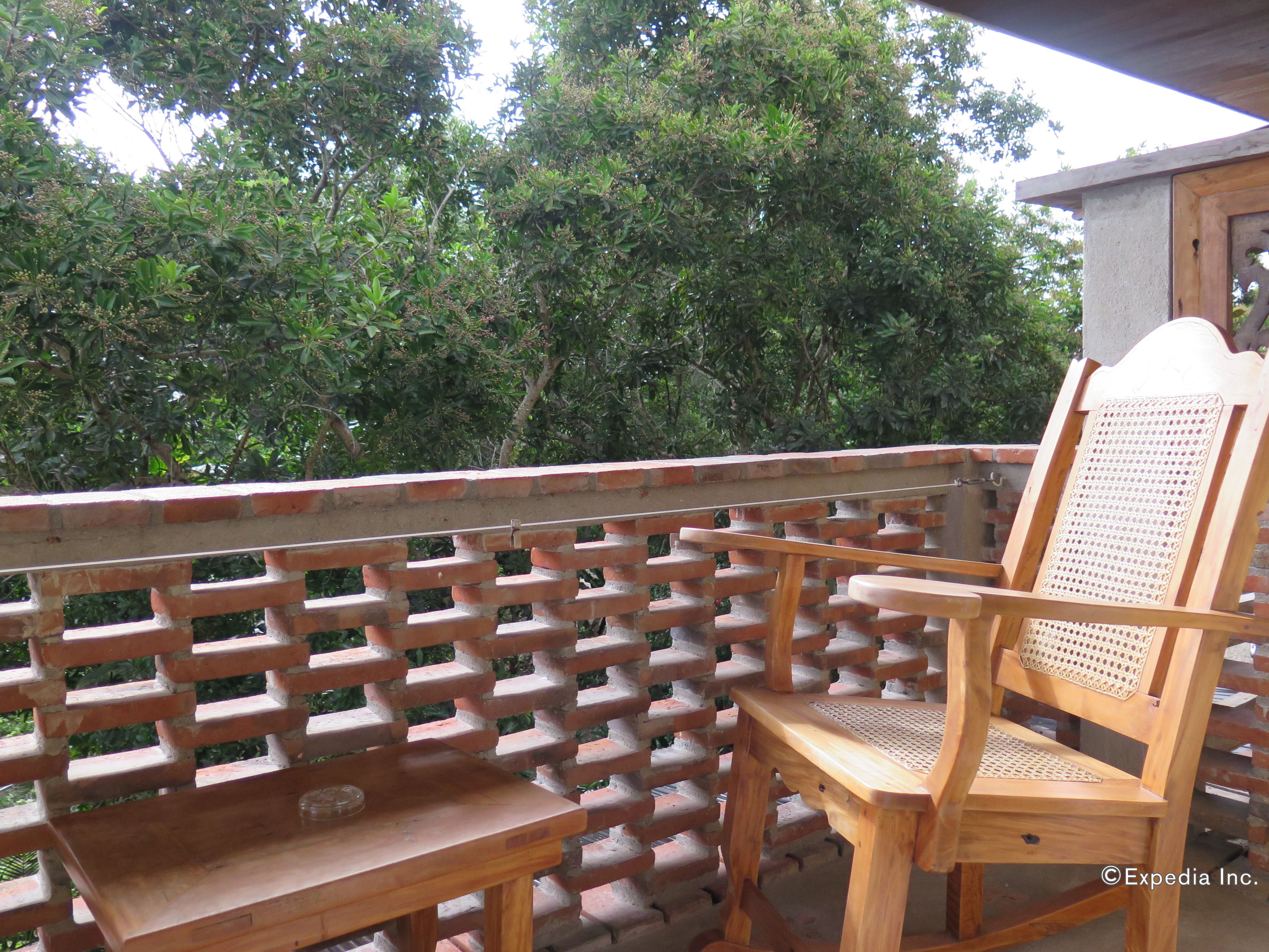 A wooden chair and table on a balcony with a brick lattice railing, surrounded by lush greenery.
