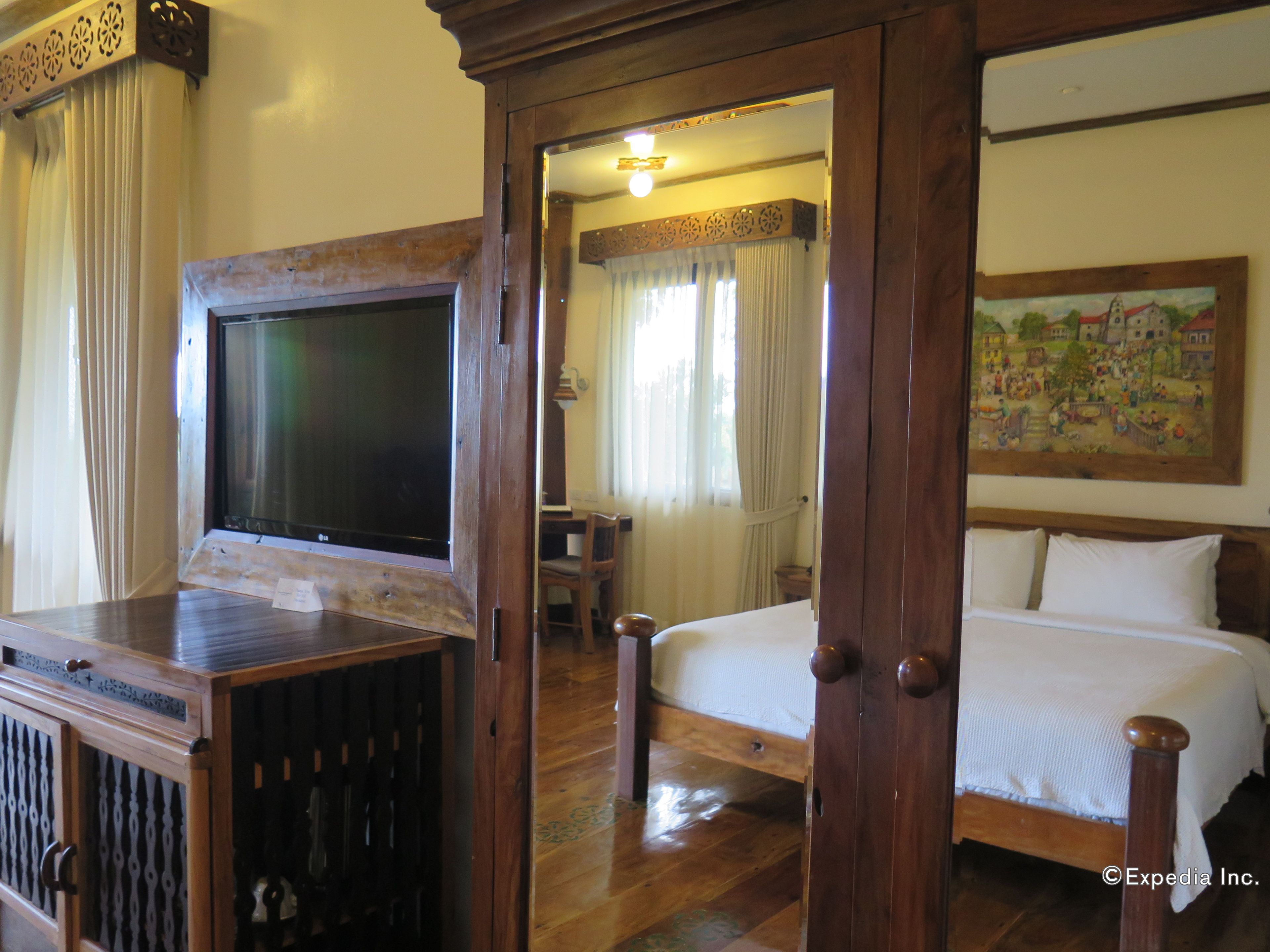 A traditional wooden room with a bed, a television, and a painting on the wall.