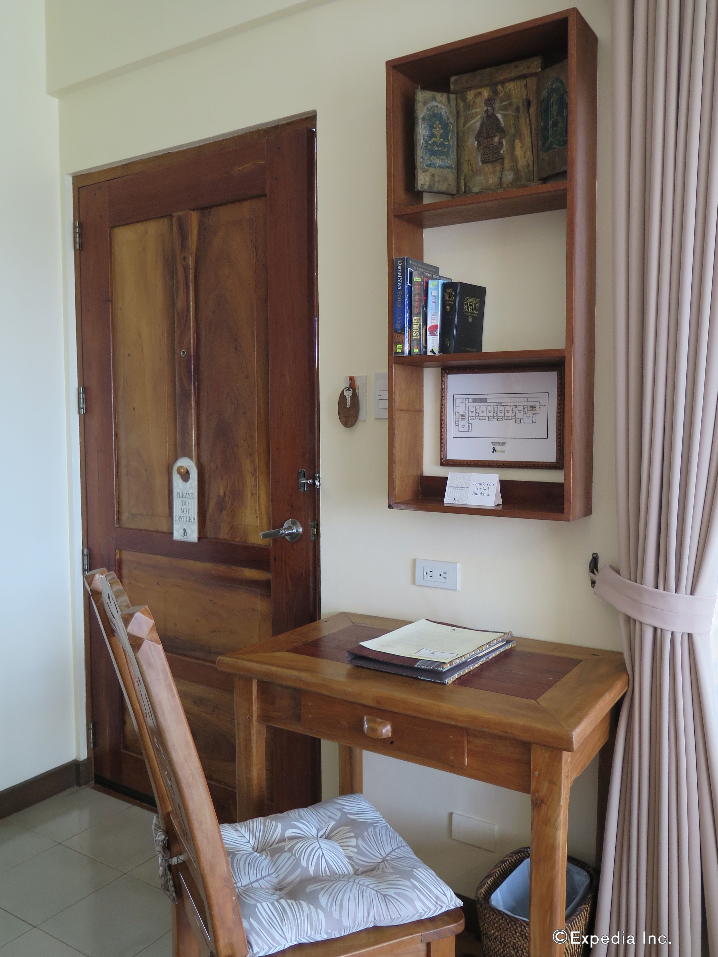 A wooden desk with a cushioned chair, a bookshelf with books and a framed map, and a door with a 'Please do not disturb' sign.