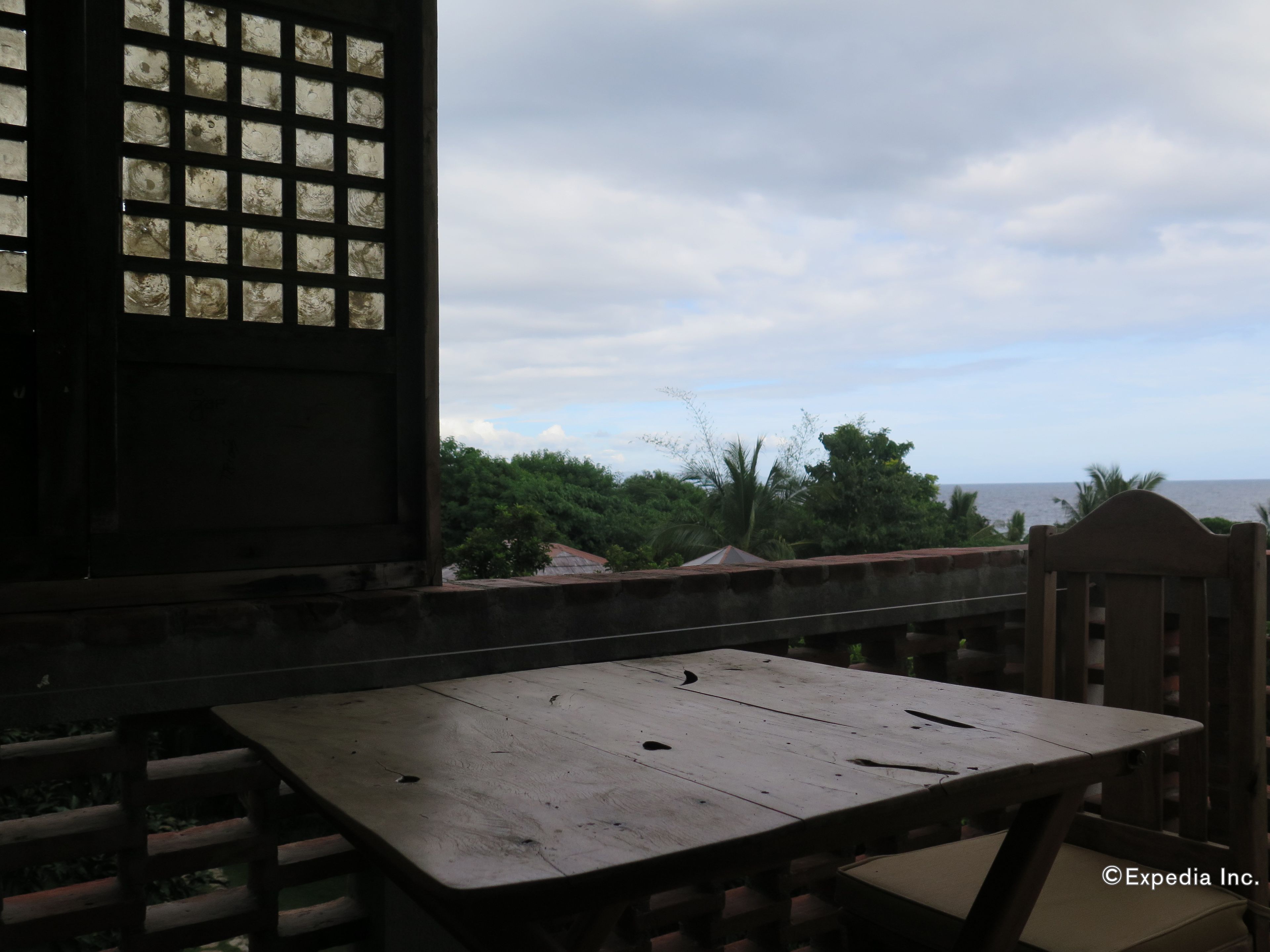 Una mesa y sillas de madera en un balcón con vistas al mar y a árboles.