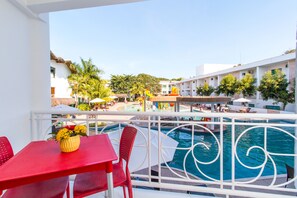 Un balcón con mesa y sillas rojas, con vistas a una piscina y una zona de juegos infantiles.