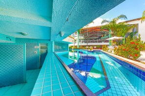 Una piscina con baldosas azules, una sauna y vistas a un edificio con balcones y plantas.