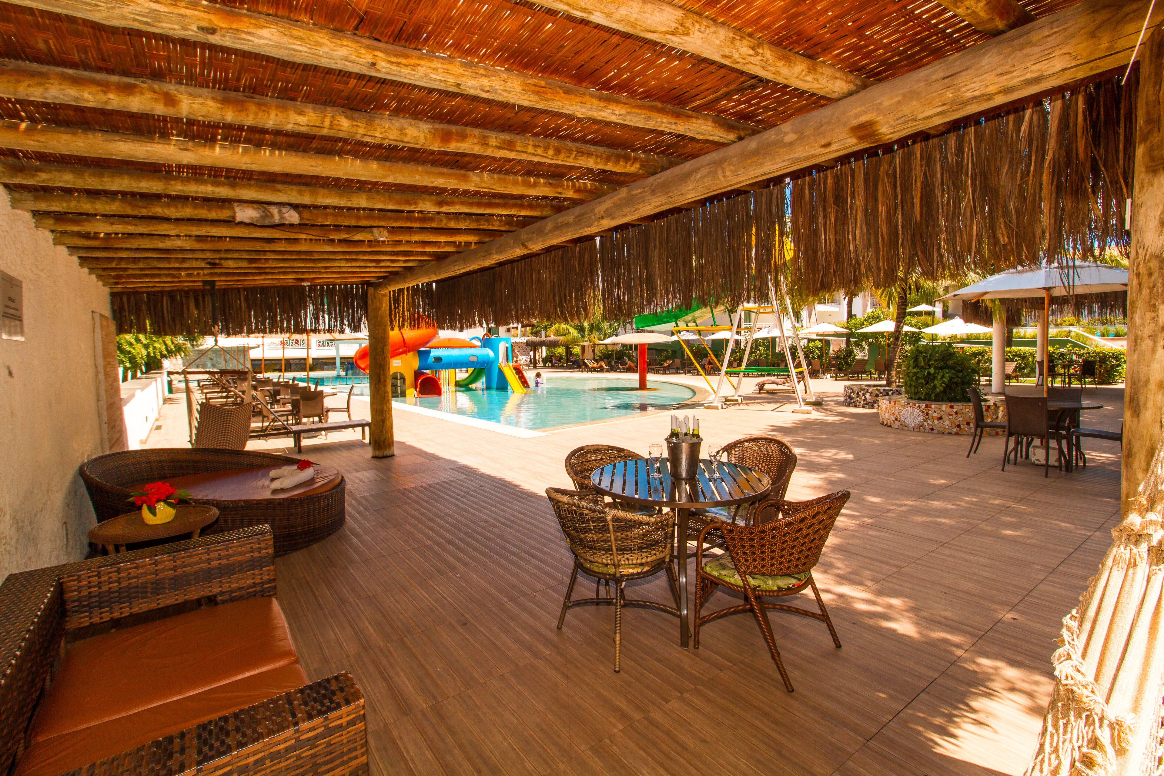 An outdoor pool area with a wooden deck, wicker furniture, and umbrellas.