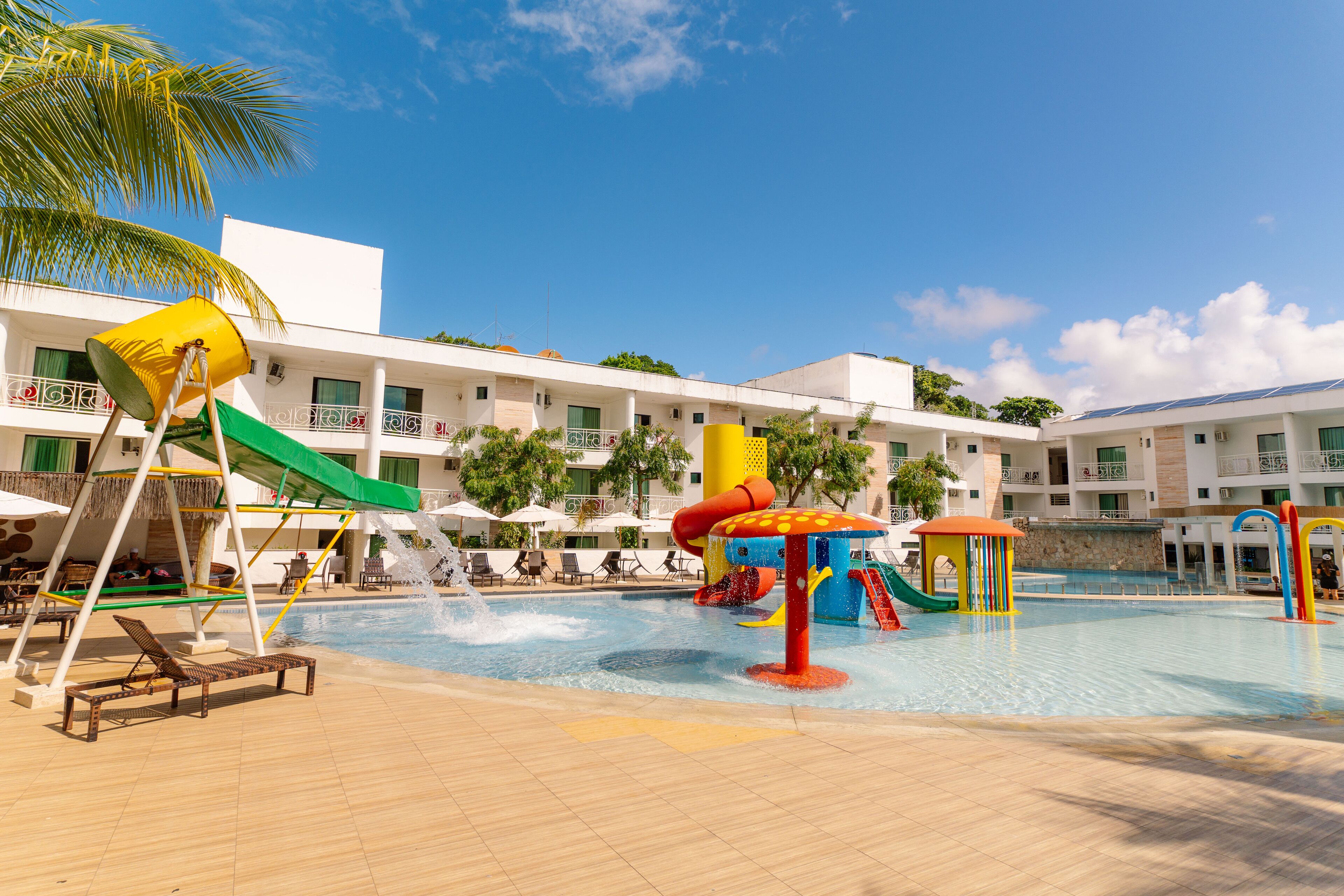 A swimming pool with slides and water play structures, surrounded by lounge chairs and umbrellas.