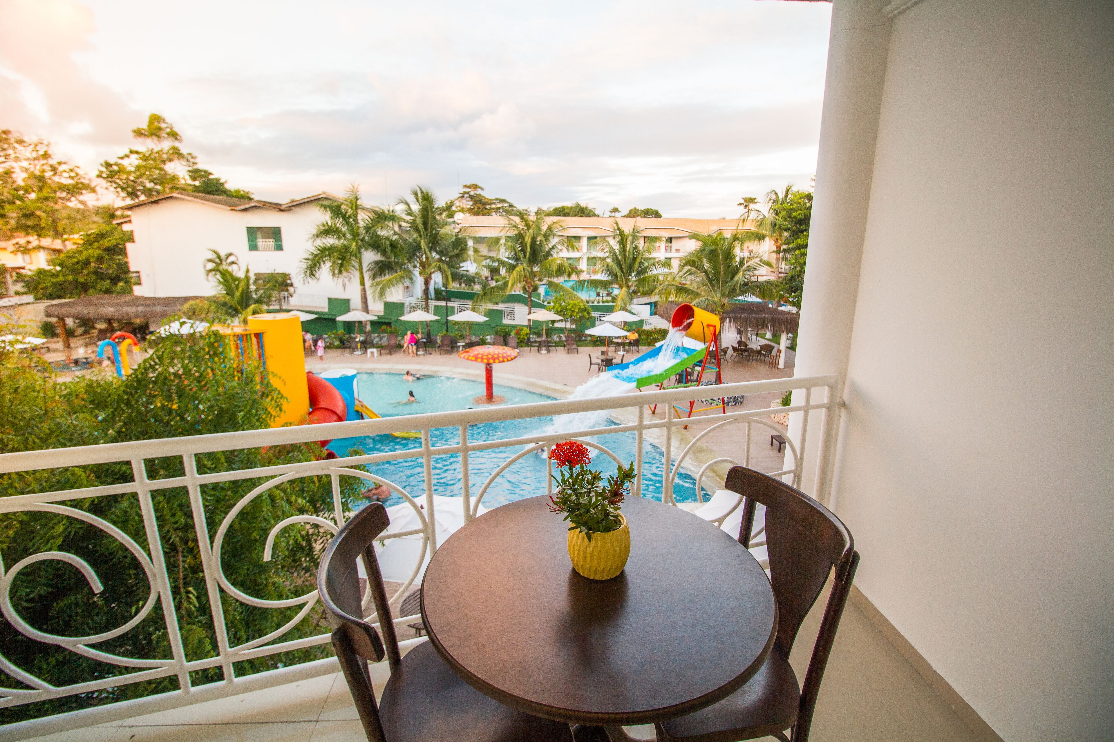 A balcony with a view of a swimming pool, palm trees, and a building in the background.
