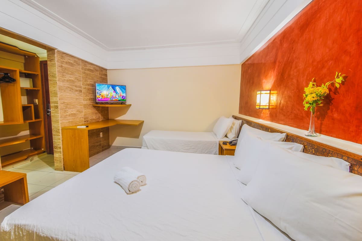 A hotel room with two beds, a TV on a shelf, a bedside table with a phone, and a wall-mounted light fixture.