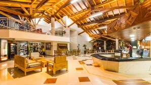 A spacious lobby with wooden furniture, a reception desk, and a mezzanine level with a railing.