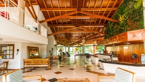 A spacious lobby with wooden furniture, a reception desk, and a green vertical garden.