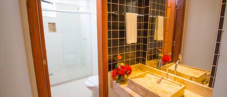 A bathroom with a glass shower enclosure, a white toilet, and a vanity with a mirror, sink, and a vase of flowers.