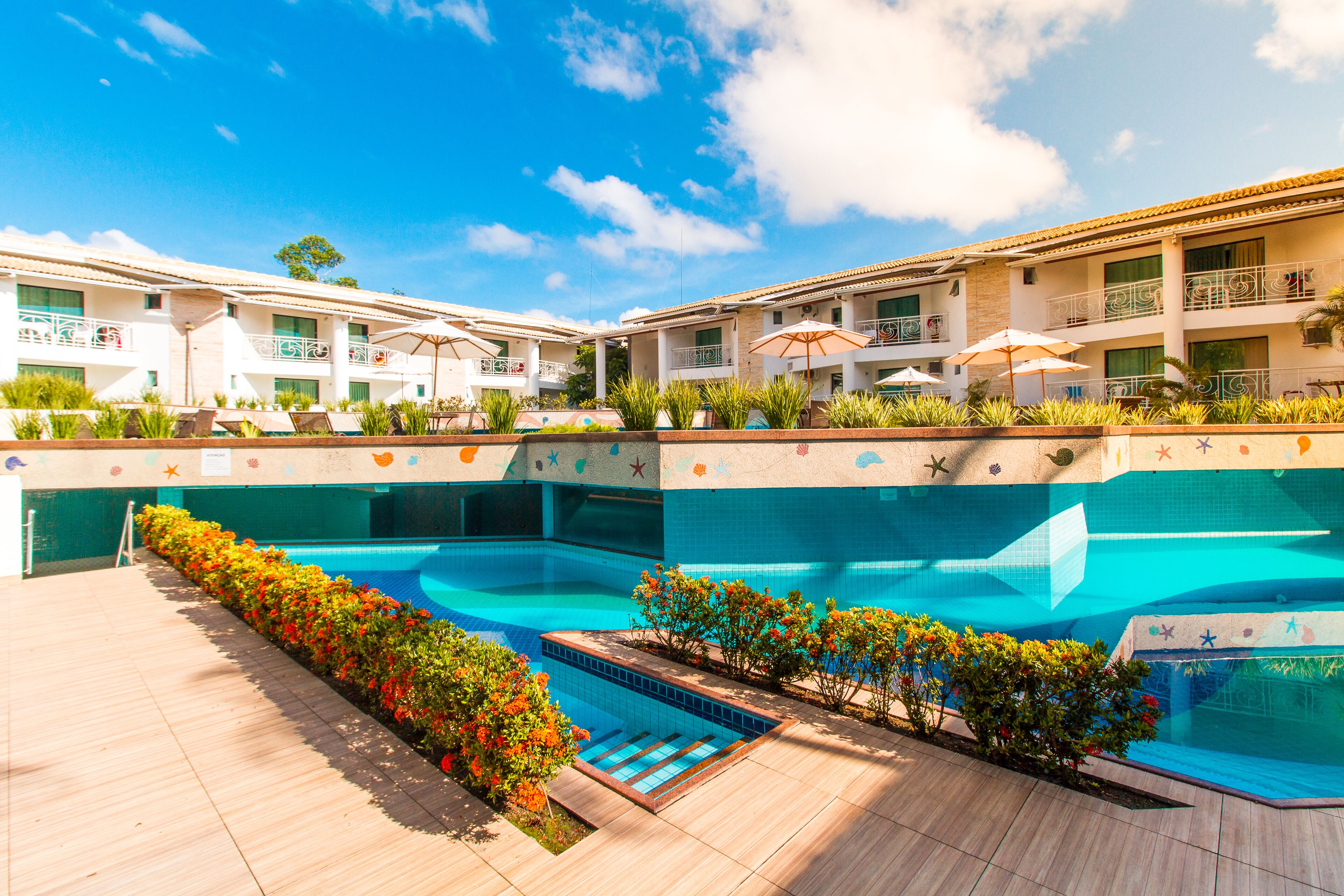 A hotel with a swimming pool, outdoor seating, and a clear blue sky.