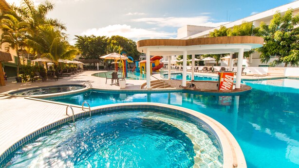 A pool area with multiple swimming pools, lounge chairs, umbrellas, and a water slide.
