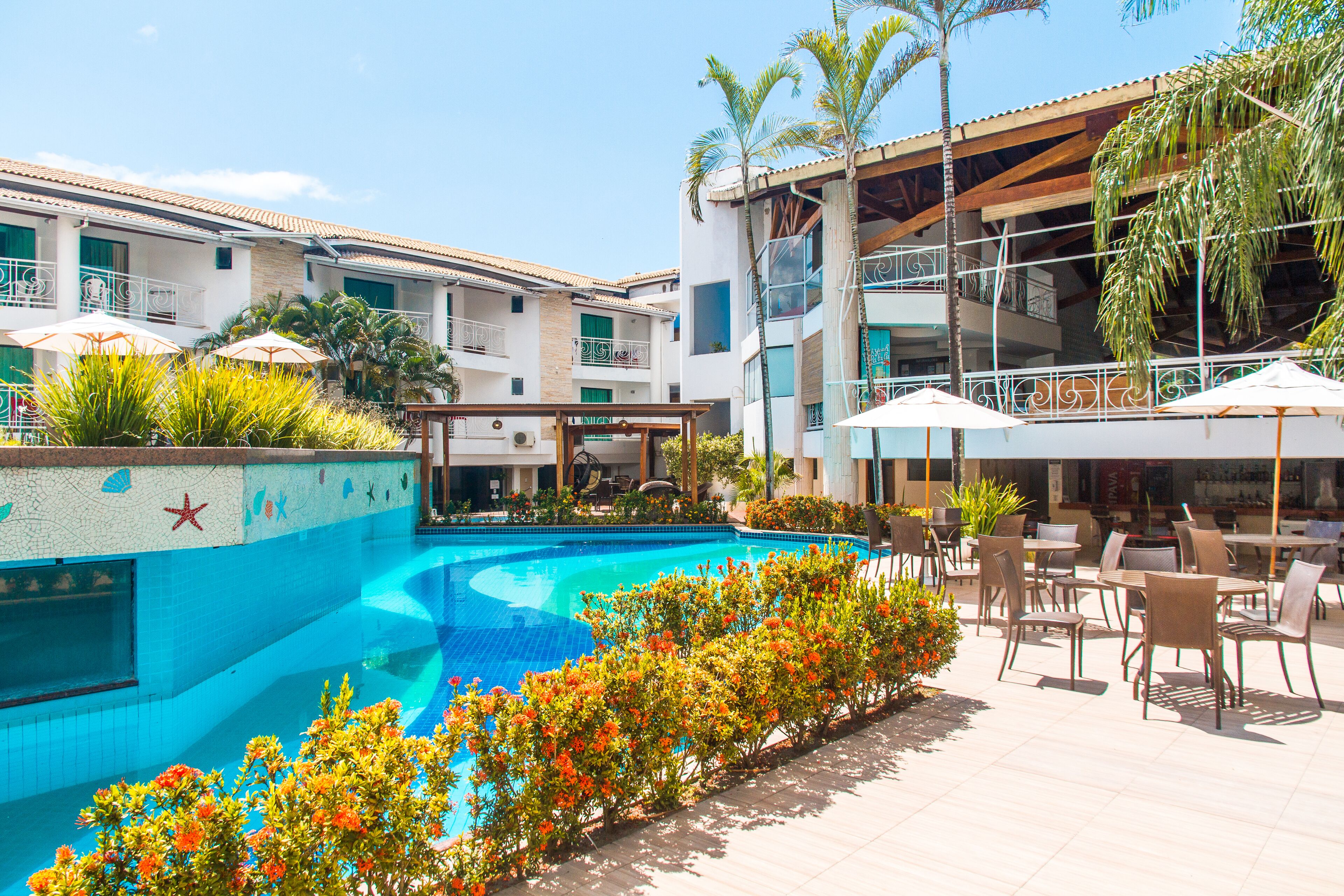 A pool area with a tiled pool, surrounded by outdoor seating and palm trees.