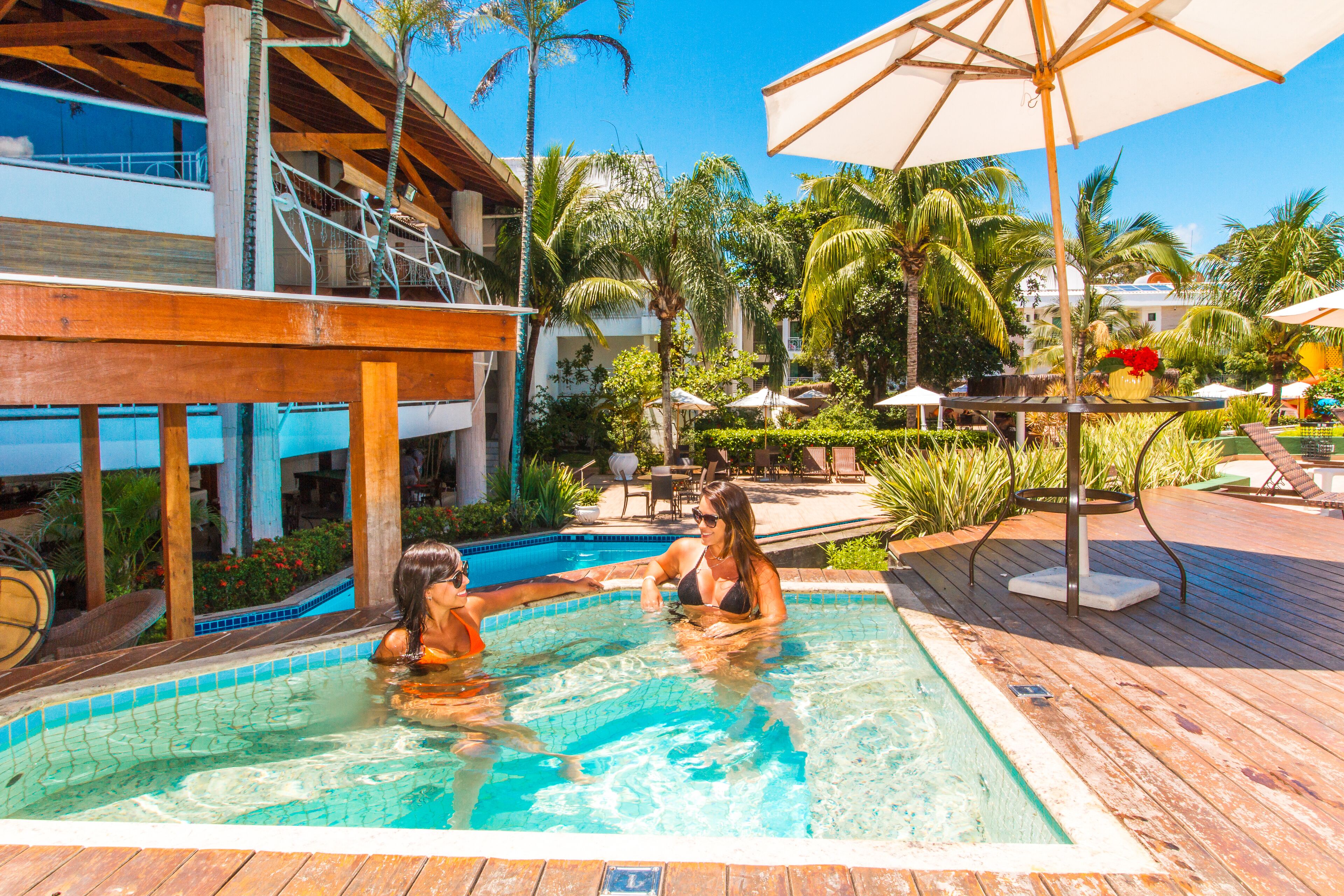 A pool area with wooden decking, lounge chairs, and umbrellas.