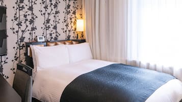 A hotel room with a bed, a nightstand, a lamp, and a window with curtains.