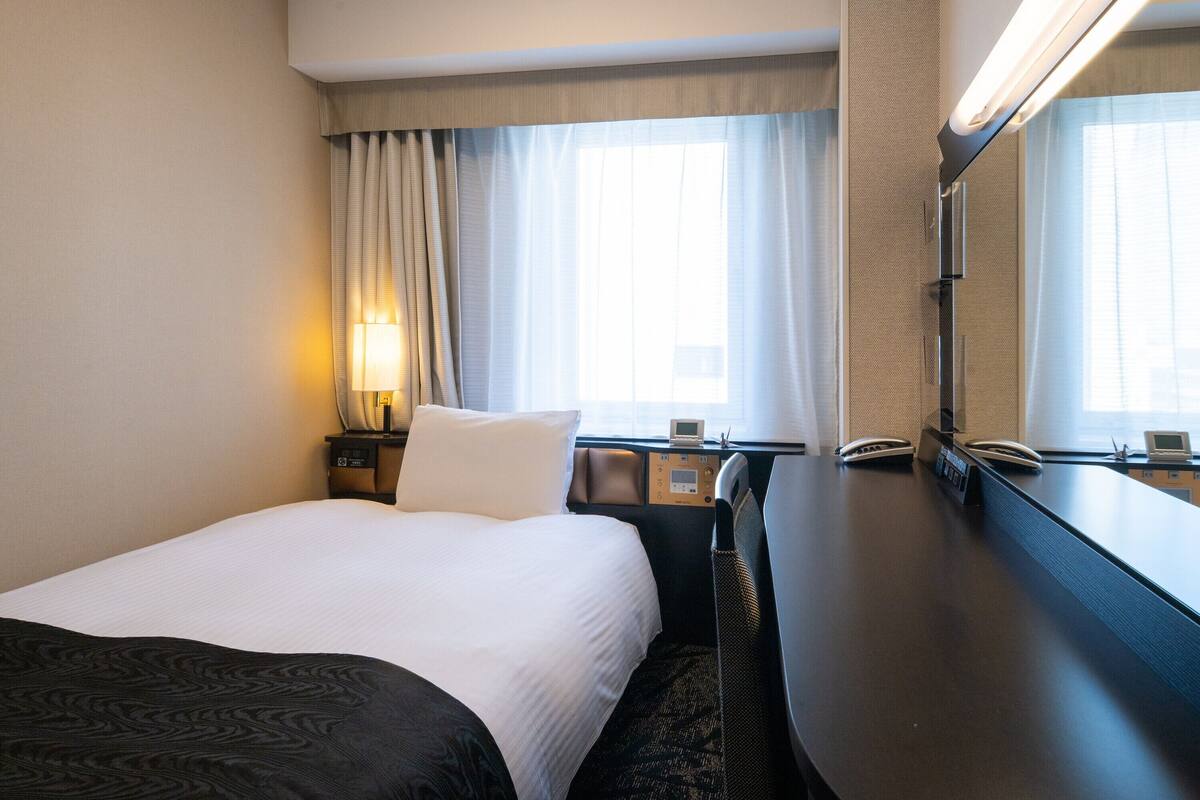 Ein Hotelzimmer mit Bett, Nachttisch, Lampe und einem großen Spiegel.