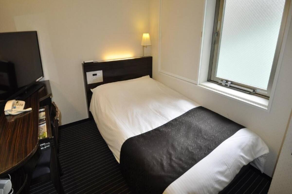 Ein Hotelzimmer mit einem Bett, einem Schreibtisch mit Telefon, einer Lampe und einem Fenster.