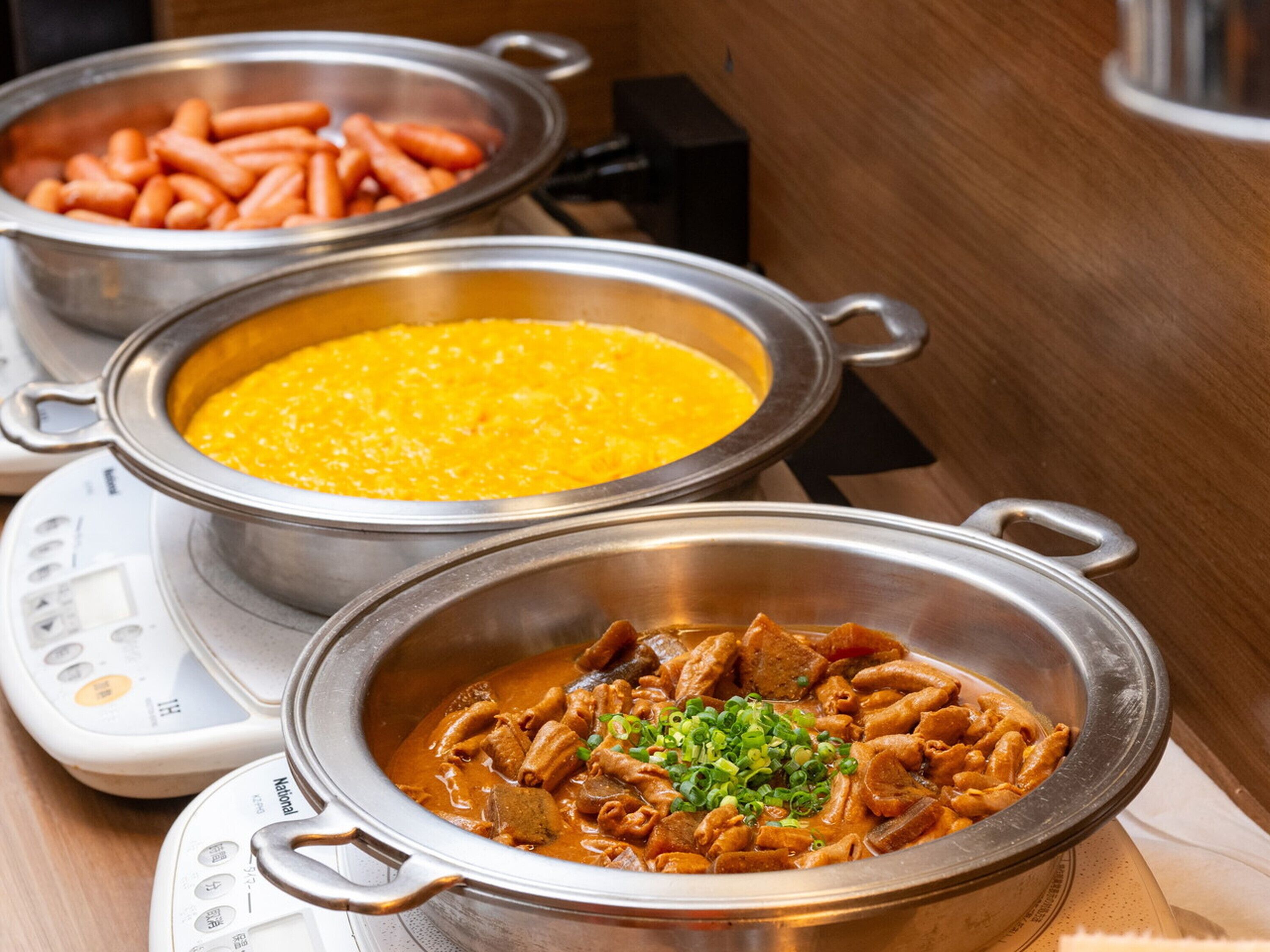 Three metal pots with different dishes on a table, a weighing scale, and a wooden surface.