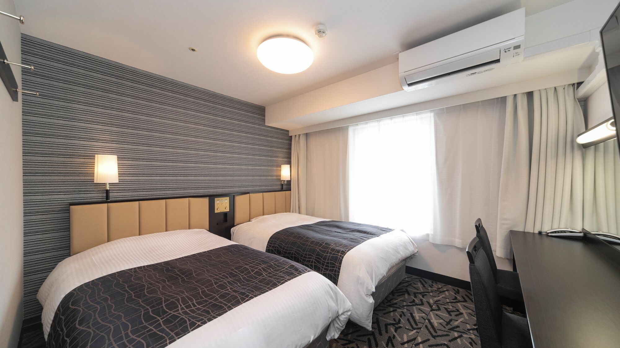 Une chambre d’hôtel avec deux lits, un bureau, un climatiseur et une fenêtre avec des rideaux.