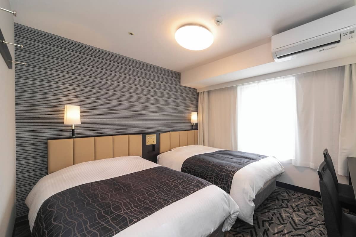 Une chambre d’hôtel avec deux lits, un bureau, un climatiseur et une fenêtre avec des rideaux.