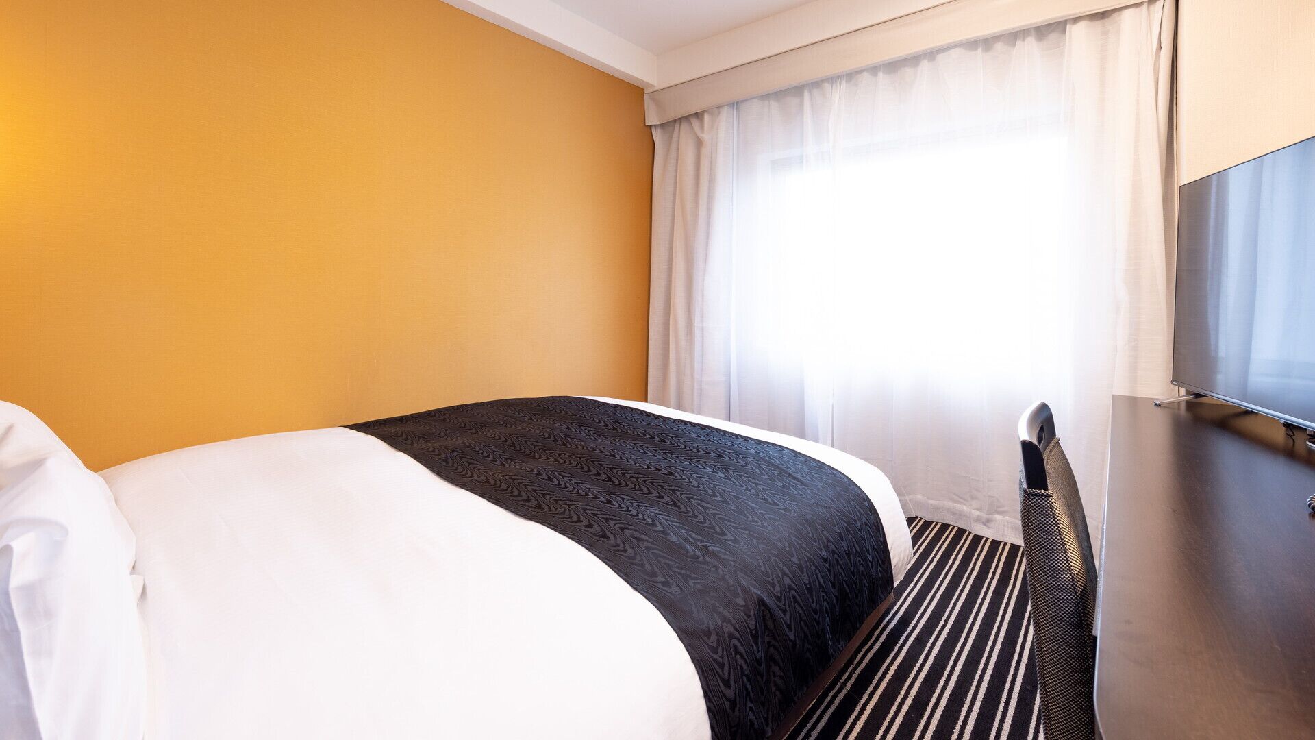 Quarto de hotel com uma cama, televisão e janela com cortinas.