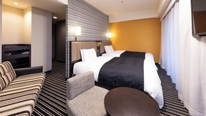 A hotel room with a large bed, a sofa, a small table, and a TV.