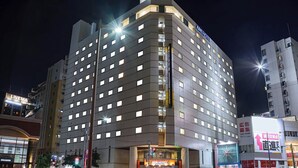 A multi-story hotel with a prominent 'APA HOTEL' sign, featuring a modern architectural design with a corner location.