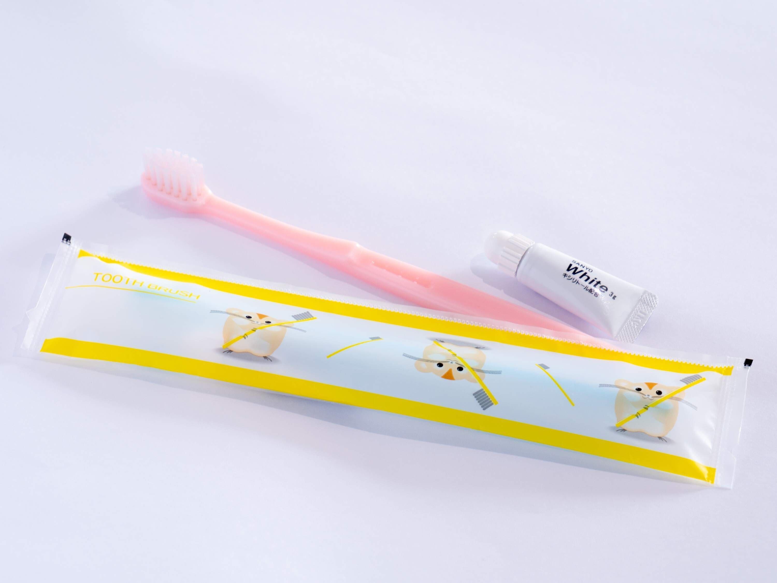 A tube of toothpaste and a toothbrush with a yellow and white packaging.
