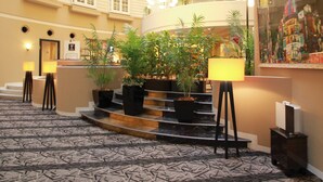 A hotel lobby with a curved staircase, potted plants, and a large painting on the wall.