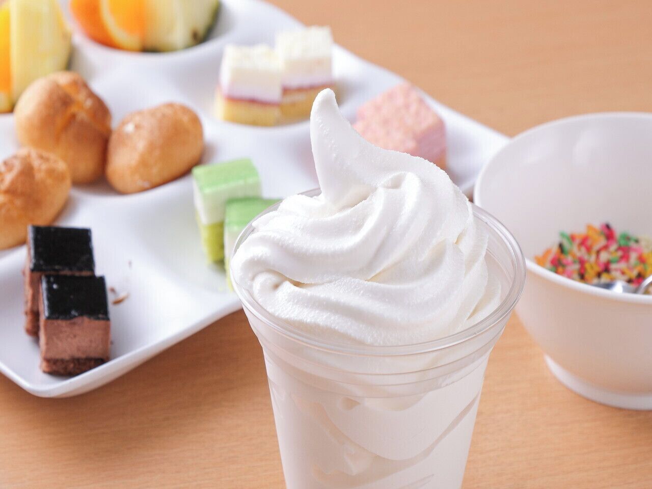A dessert table with various sweets and a glass of whipped cream.