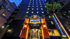 Una entrada de hotel moderna con un cartel llamativo, una puerta de cristal y un pequeño árbol a la derecha.
