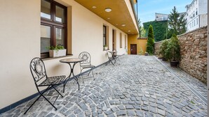 A courtyard with cobblestone flooring, outdoor seating, and potted plants. - Garni Hotel VIRGO (Bratislava)