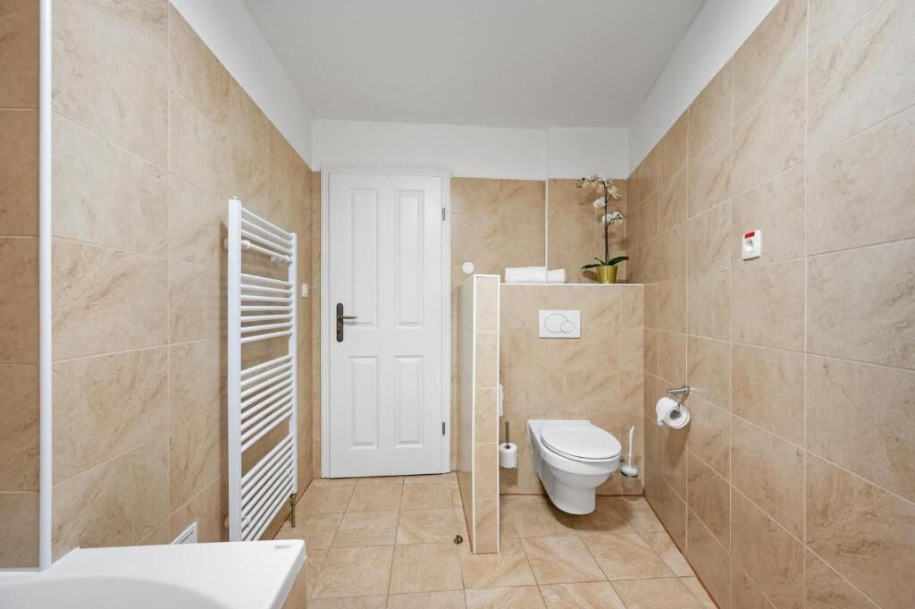 A small, compact bathroom with beige tiles, a white toilet, a towel rack, and a shower area.