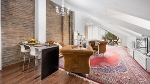 A modern loft with exposed brick walls, a dining area with bar stools, a large brown armchair, and a red patterned rug. - Garni Hotel VIRGO (Bratislava)