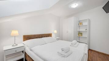 A bedroom with a bed, two bedside tables, a nightstand, a wardrobe, and a TV mounted on the wall.