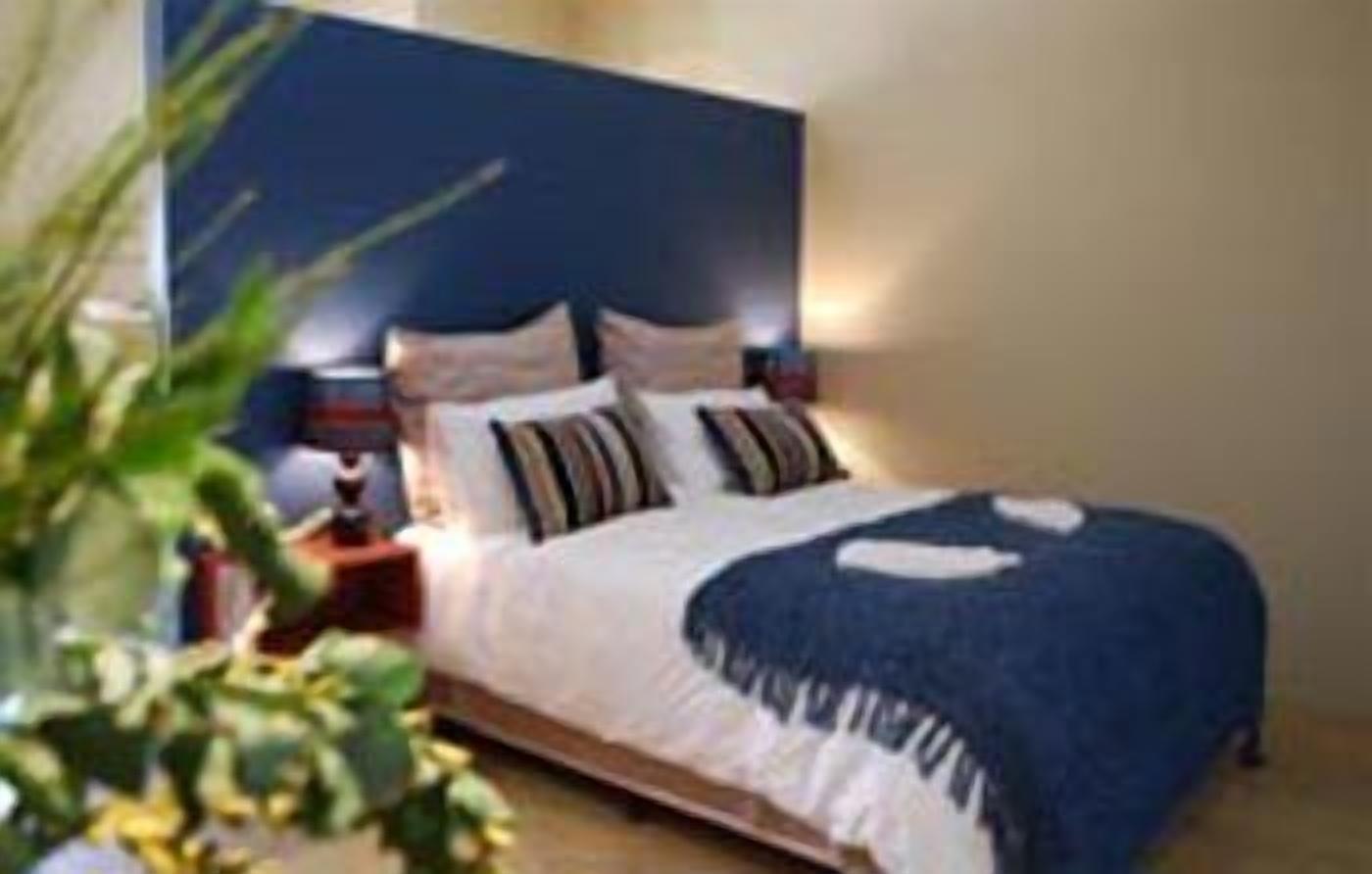 A neatly made bed with a blue and white bedspread, two pillows, and a bedside table with a lamp.