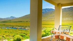 Habitación con vista a un paisaje montañoso y un pequeño cuerpo de agua. Se observa una silla y una mesa en primer plano.