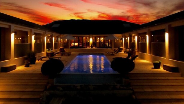 Zona de piscina con vista al atardecer, rodeada de edificios con iluminación cálida.