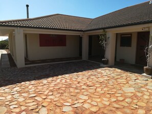 A building with a tiled roof, a stone-paved courtyard, and a red sign on the wall. - Kapensis Guesthouse (Pringle Bay)