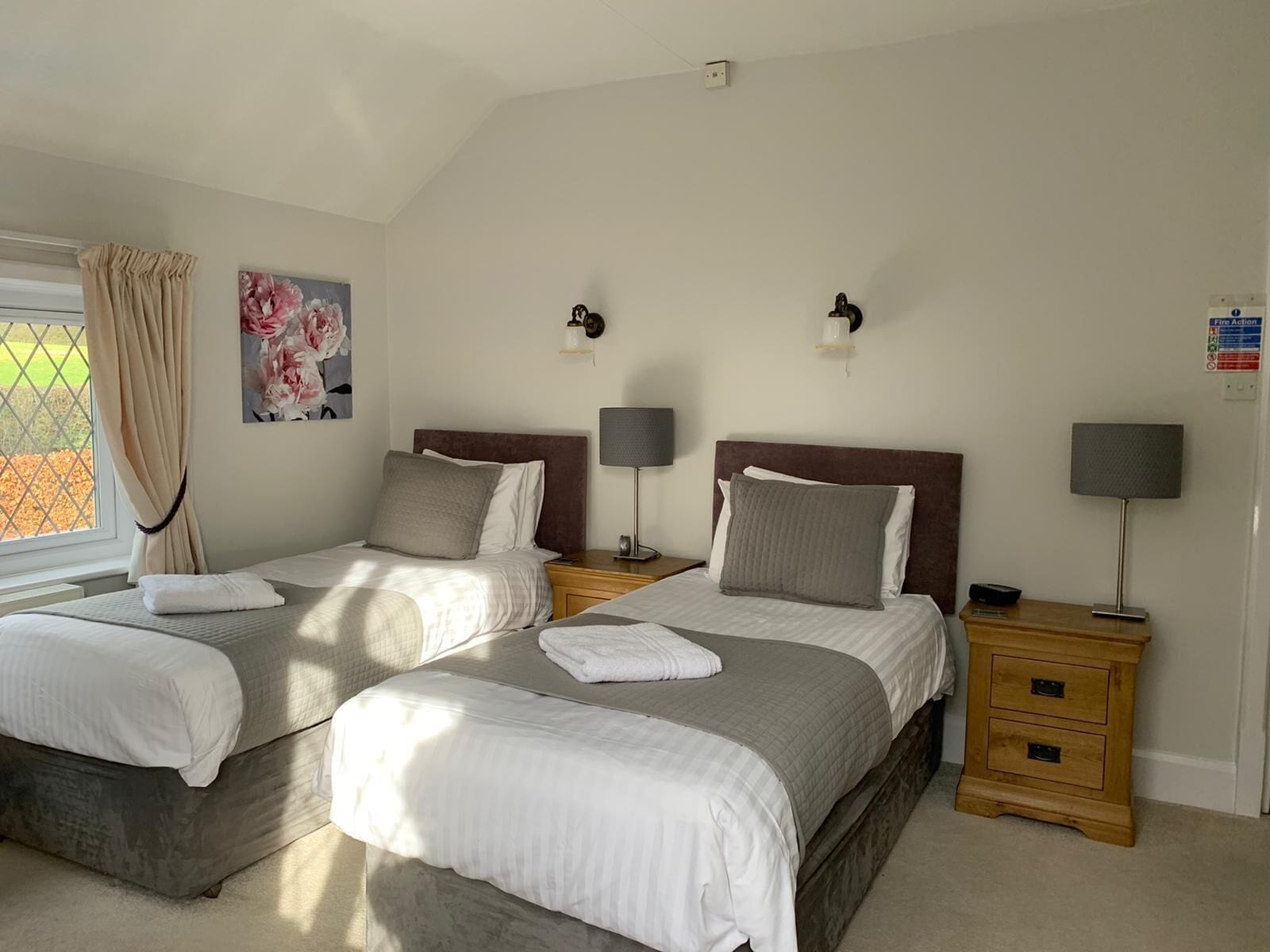 Een hotelkamer met twee bedden, een nachtkastje, een lamp en een schilderij aan de muur.