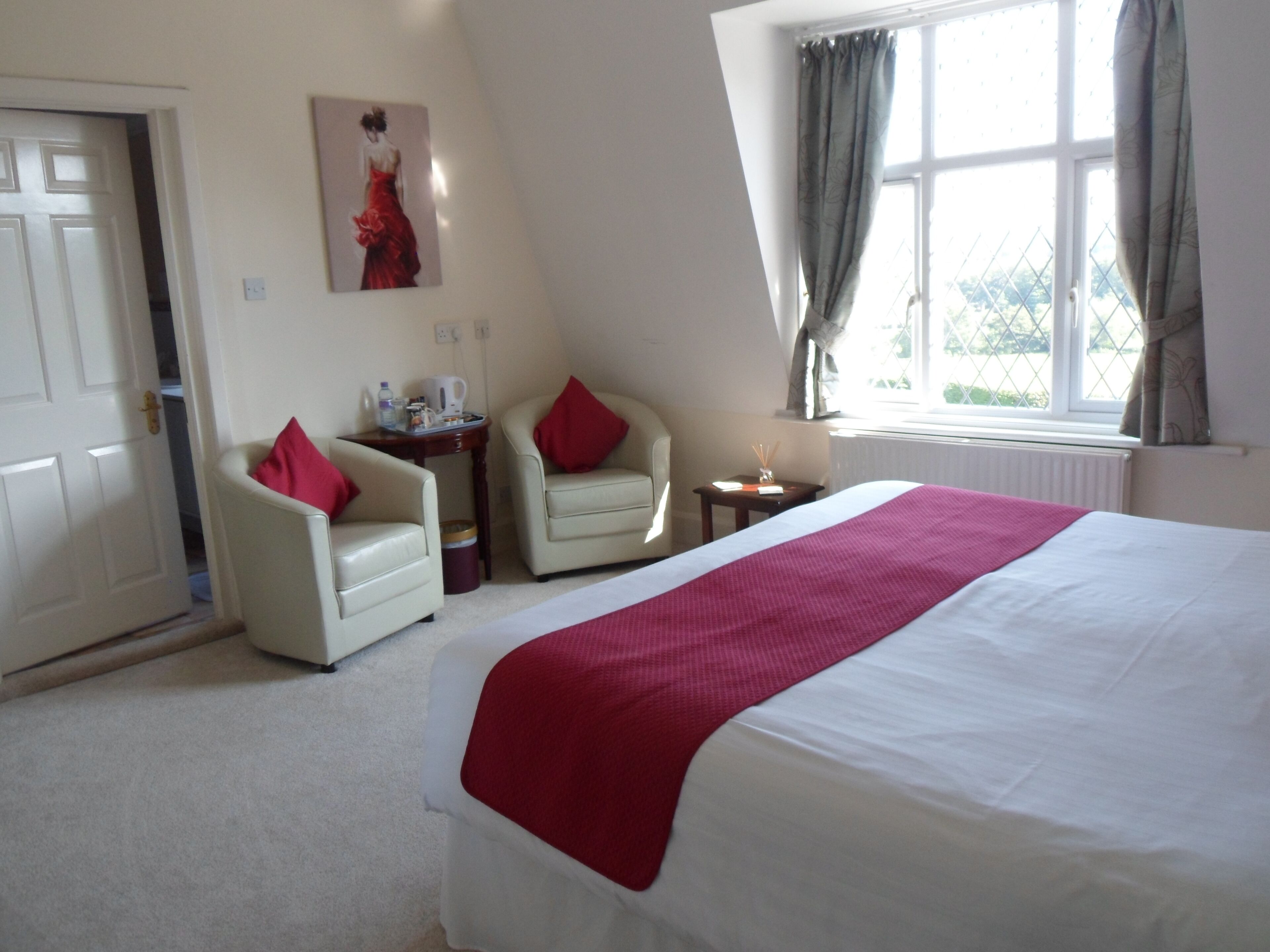 A hotel room with a large bed, two armchairs, a small table, and a window with curtains.
