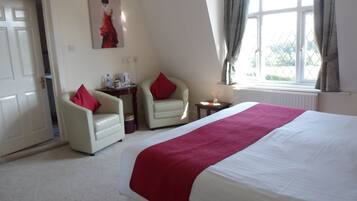 A hotel room with a large bed, two armchairs, a small table, and a window with curtains.