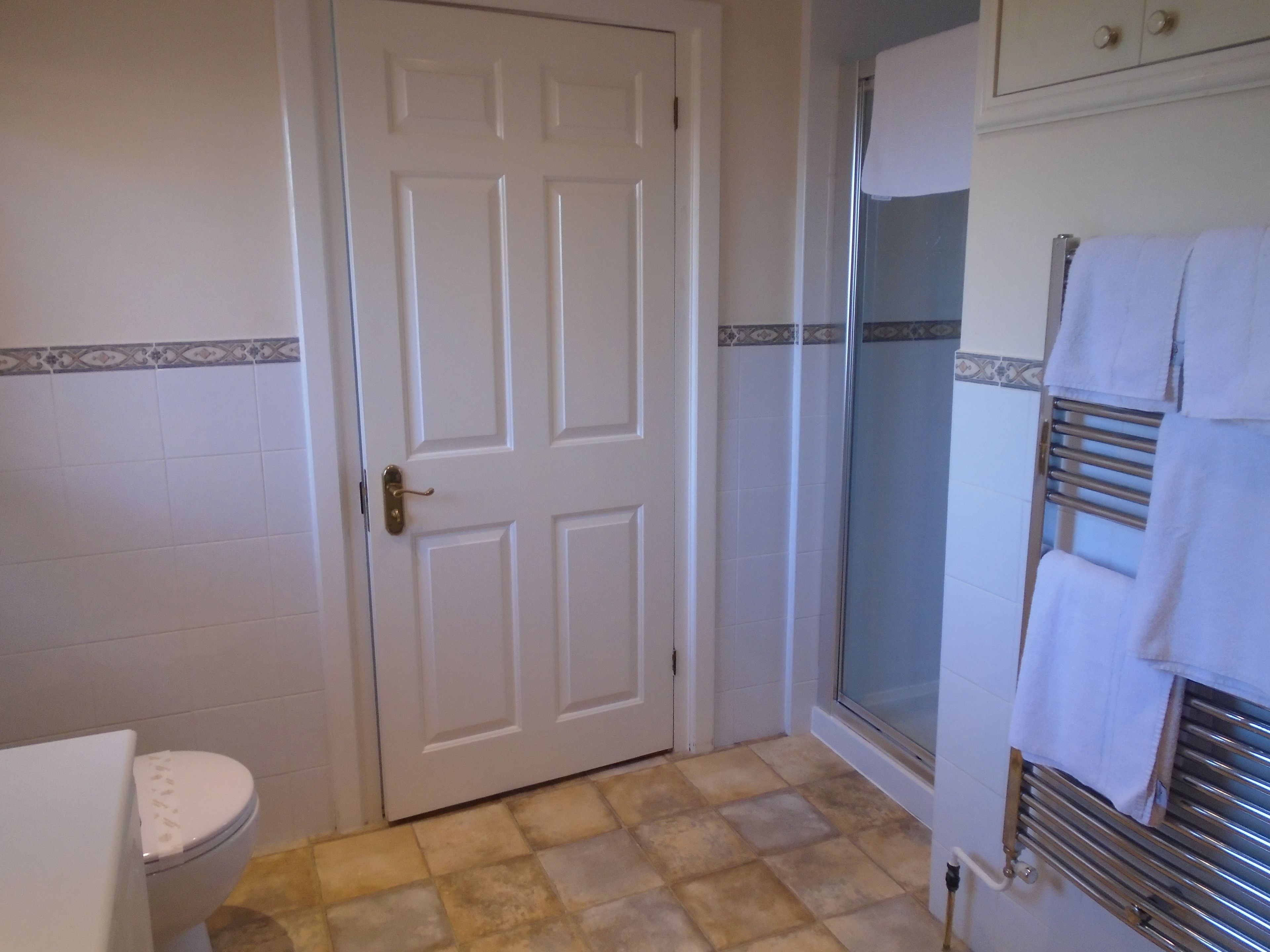A bathroom with a white door, a toilet, a shower with a glass door, and a towel rack with towels.