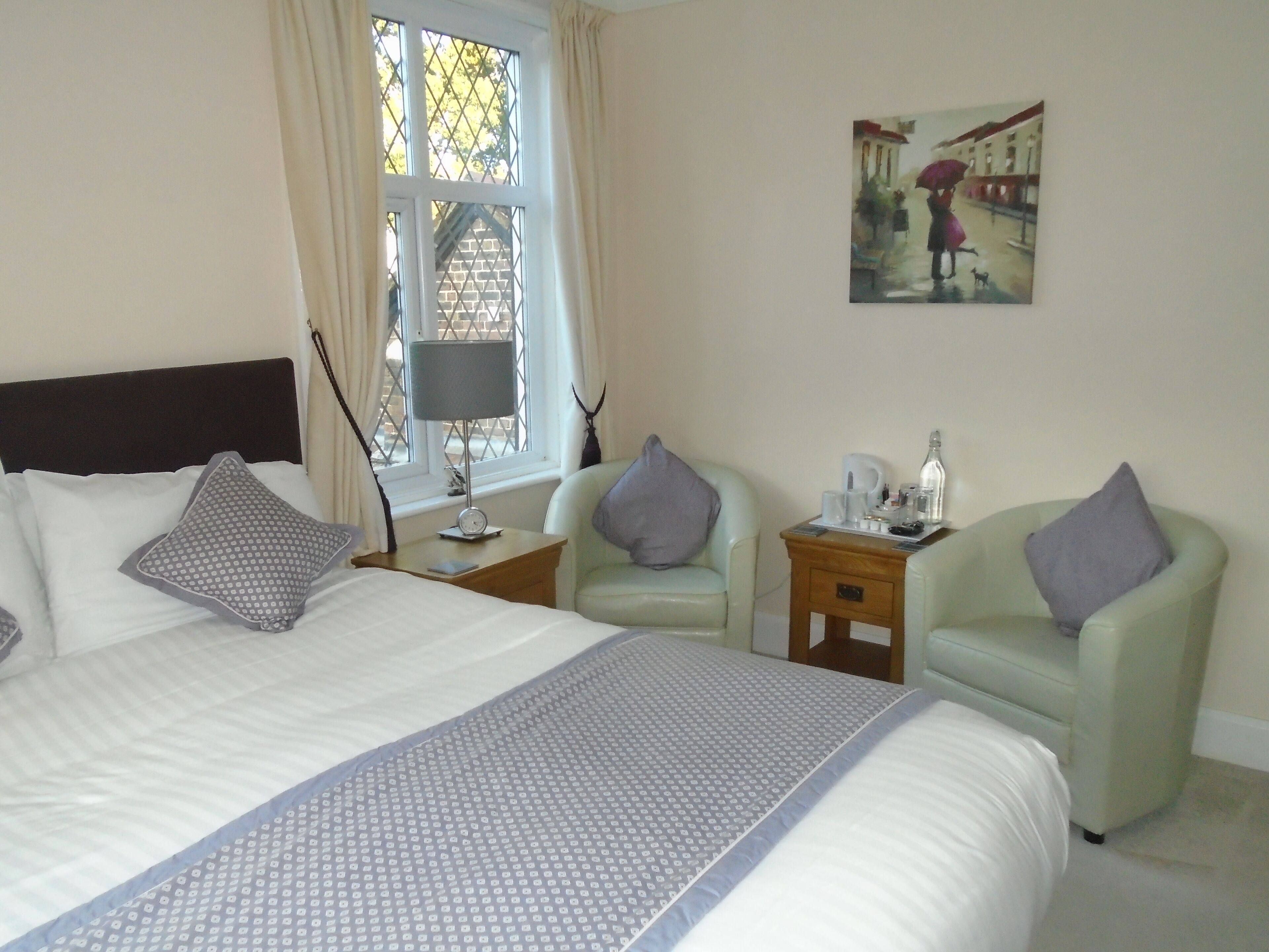 A hotel room with a large bed, two armchairs, a small table with a lamp, and a painting on the wall.