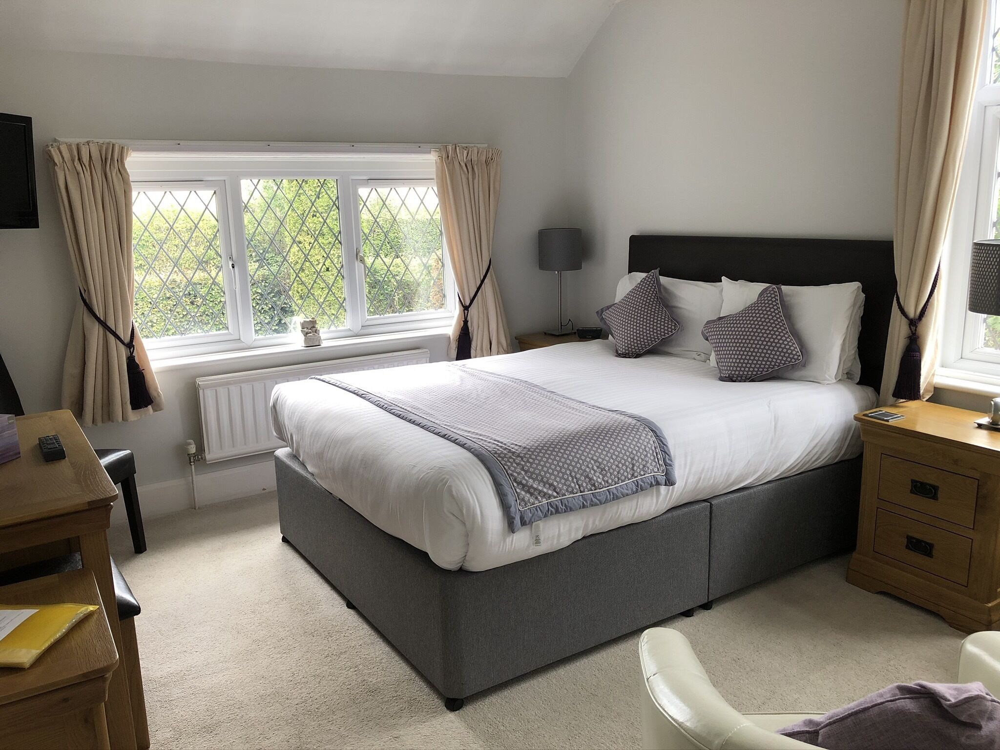 A bedroom with a large bed, bedside tables, a desk, and a window with curtains.