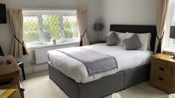A bedroom with a large bed, bedside tables, a desk, and a window with curtains.