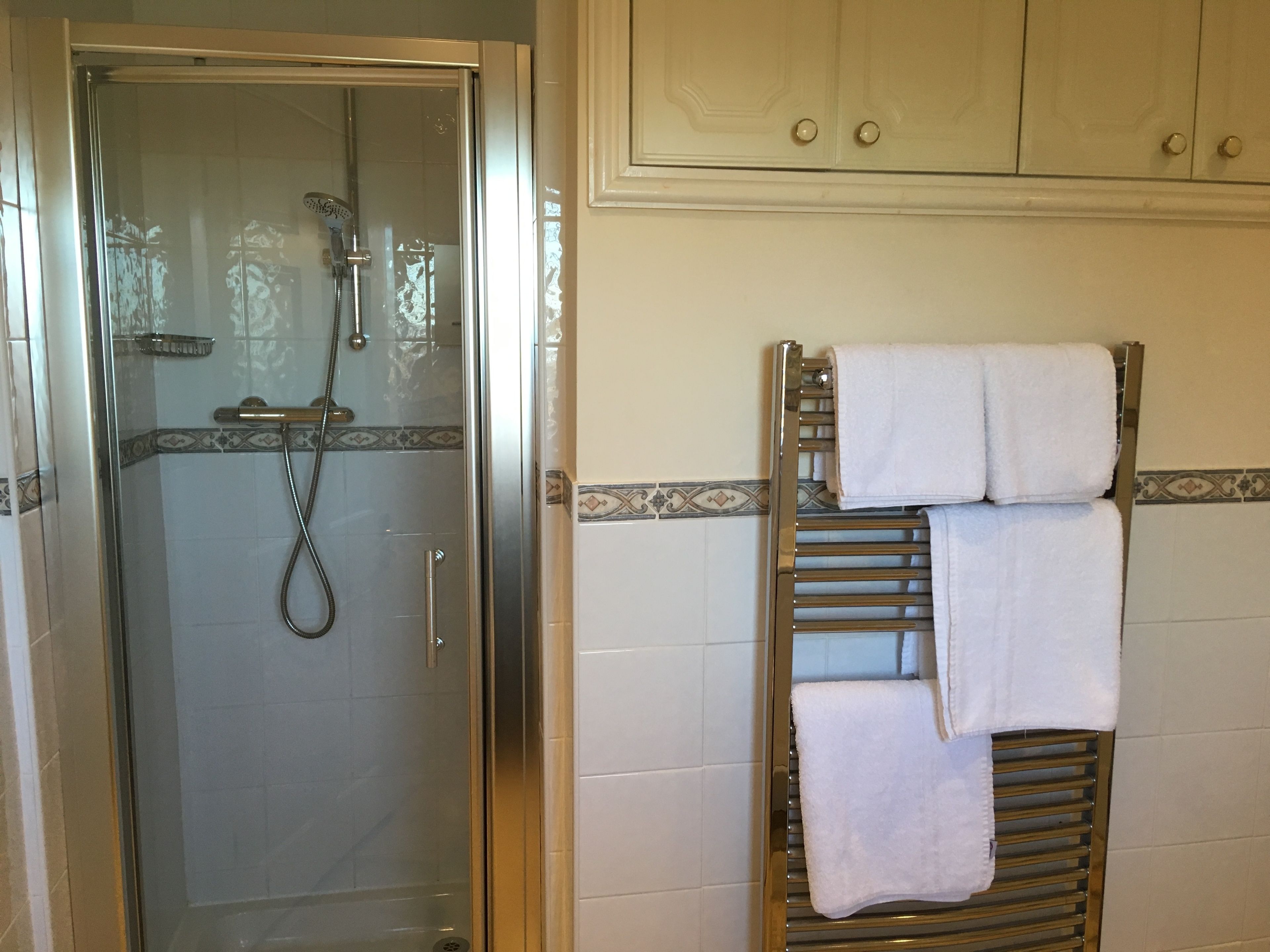 Une salle de bain avec une douche à parois de verre, un porte-serviettes muni de plusieurs serviettes et des murs carrelés.