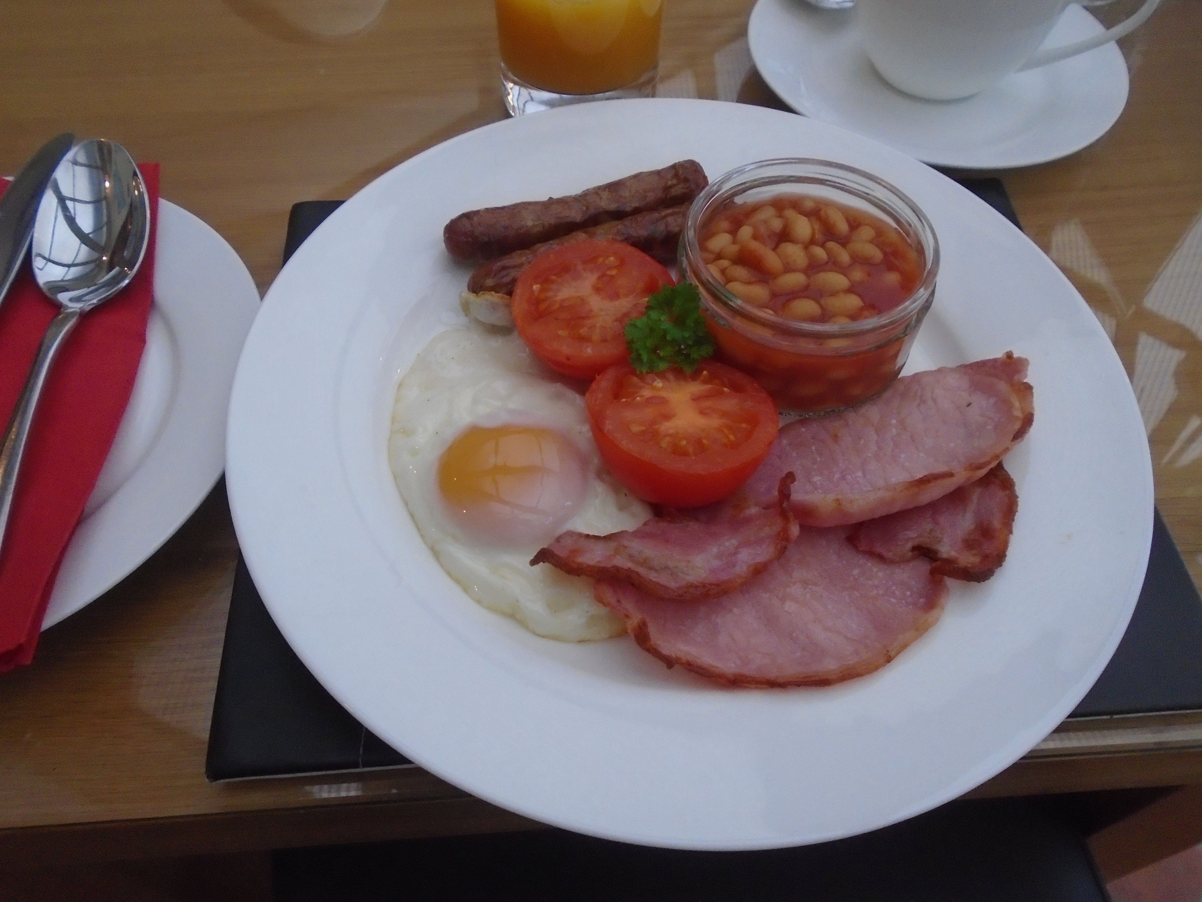 A breakfast plate with eggs, bacon, tomatoes, beans, and sausages.